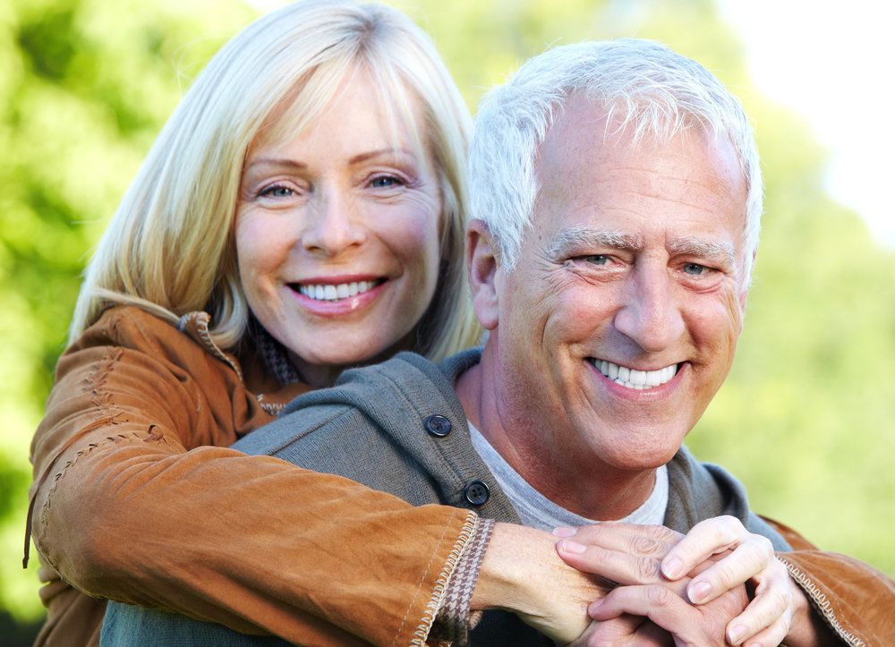 Smiling older couple with woman wrapping arms around man's shoulders